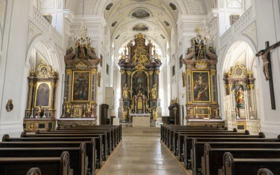 Gold statues and oil paintings adorn the front of a traditional Catholic church with wooden pews