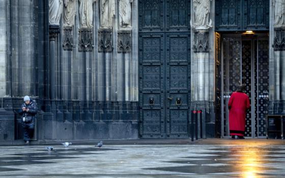 Two people are outside a cathedral with statues and ornate doors in a shiny square with pigeons