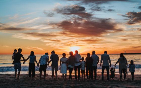 A photo taken at sunset of a family gathered by the shore (Unsplash/Tyler Nix)