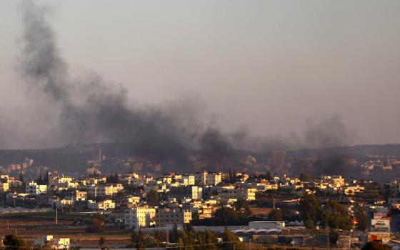 Black smoke billows above buildings and trees set against a dark gray sky