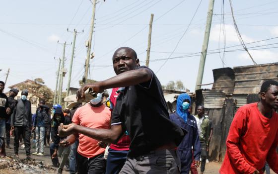 A Black man holds his hands back while carrying a rolled up paper. Other Black men, many wearing surgical masks, surround him.