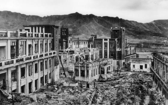 A black and white photo of the ruins of buildings. Some are in rubble and some are still standing.