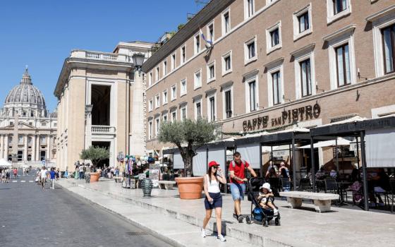 Tourists walk down a commercial street where St. Peter's Basilica is visible at the end