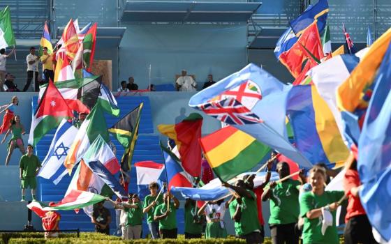 Pope Francis, on stage, looks over the procession of flags from the all the countries represented by young people participating in World Youth Day during the event's welcome ceremony at Eduardo VII Park in Lisbon, Portugal, Aug. 3. (CNS/Vatican Media)