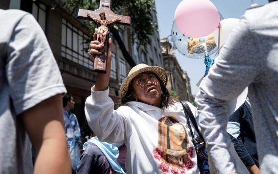 A woman wearing a shirt with the Virgin Mary on it holds a crucifix above her head while in a crowd