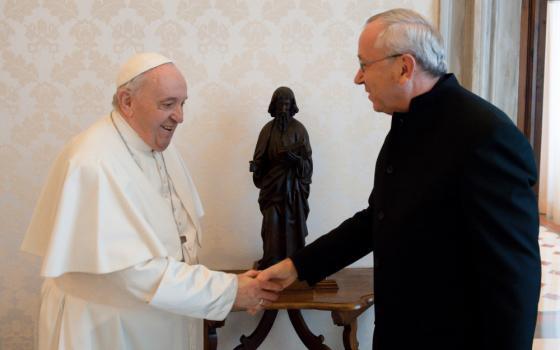 Pope Francis shakes the hand of a white man wearing glasses and a black garment