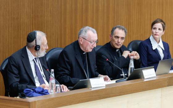 A man wearing a kippah sits next to two men wearing Catholic clerical shirts and a woman in Western business attire