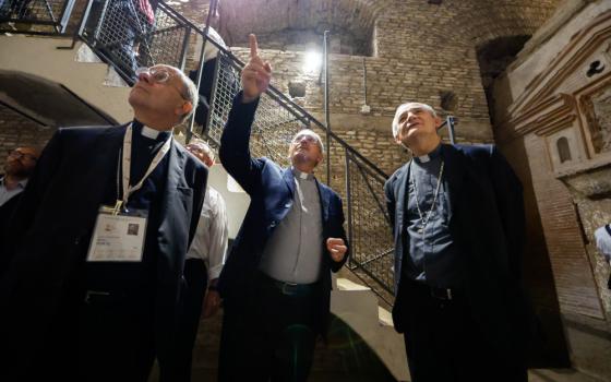 Three white men wearing clerical collars look up at the ceiling of an underground stone-lined space