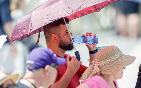 A man cools off from the heat under an umbrella as he drinks water while visitors wait for the start of Pope Francis' Angelus prayer in St. Peter's Square at the Vatican July 9, 2023. (CNS photo/Lola Gomez)