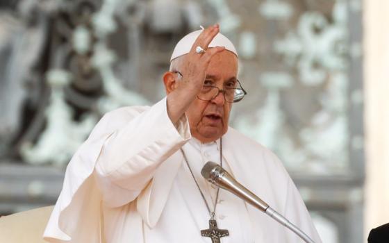 Pope Francis raises his right hand as he speaks into a microphone