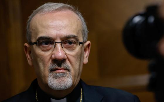 A light-skinned man with a white beard wearing glasses looks at the camera