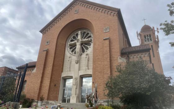 The outside of a high-ceilinged Catholic church with a crucifix on the facade and flowers around the entrance