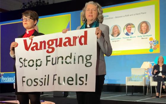 GreenFaith organizers Chelsea MacMillan, left, and Amy Brooks Paradise hold up a banner that reads, "Vanguard Stop Funding Fossil Fuels!" during an Oct. 23 investment industry conference at the Omni La Costa Resort in Carlsbad, California. (Courtesy of GreenFaith)