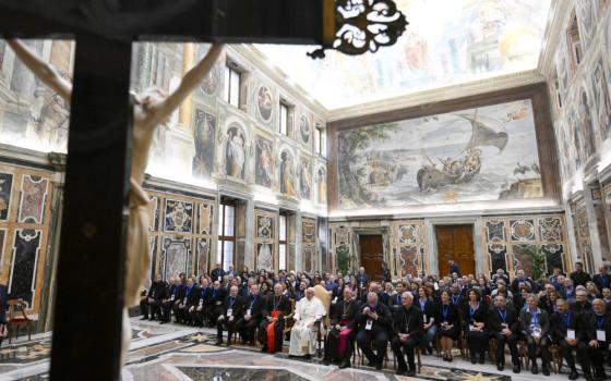 A group photo with Pope Francis in the middle is visible from behind a crucifix