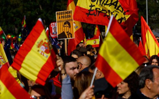 A crowd of people hold up Spanish flags in the dark. One flag has writing on it. 