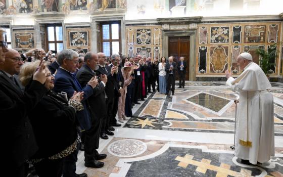 Pope Francis waves at an assembled crowd of lay people while using a cane inside