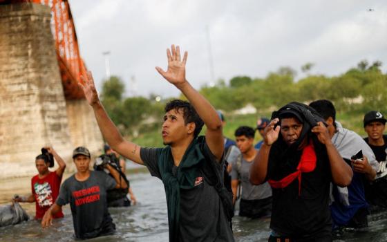 Several people stand in river. One man's hands are raised as if praising God. 