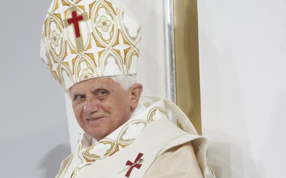 Pope Benedict XVI wears a white and gold mitre with a red cross on it and matching vestments