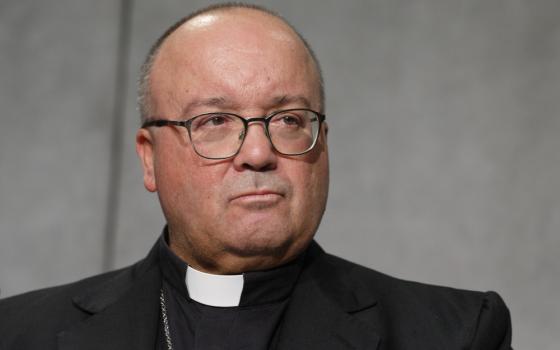 A white man with a buzz cut wears glasses, a clerical collar and a pectoral cross