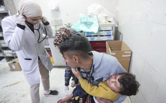 A person carries a child in distress to a medical professional. The floor of the facility looks stained, potentially with blood.