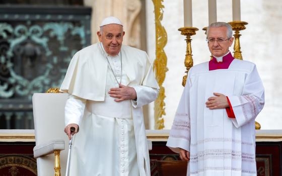 Pope Francis stands with cane smiling. 