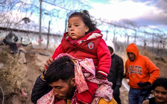 Briana, a 1-year-old migrant girl from Peru, is carried by her father, Jordan, as they search for an entry point into the United States past a razor wire-laden fence along the bank of the Rio Grande in El Paso, Texas, March 26. (OSV News/Reuters/Adrees Latif)