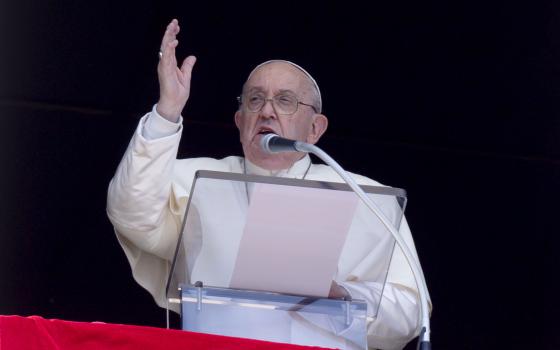 Pope Francis at lectern, above St. Peter's Square, hand raised in blessing. 