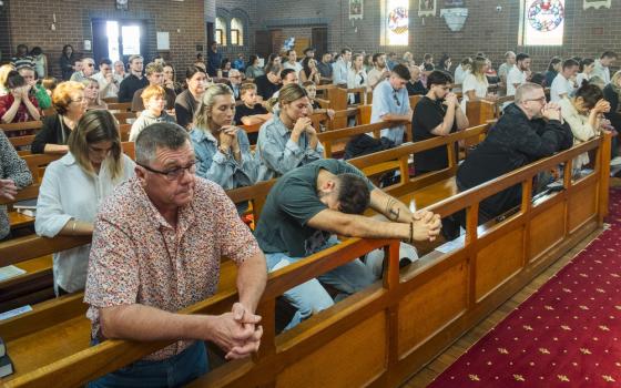 Faithful kneel in pews, praying the rosary.