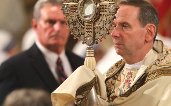 Bishop, vested, exposes Eucharistic Host in monstrance. 