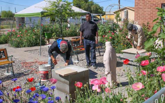 Priest and parishioners work in sunny garden.