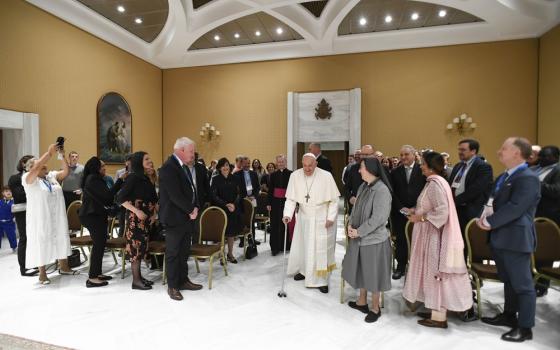 Pope Francis stands among conference attendees in large hall. 