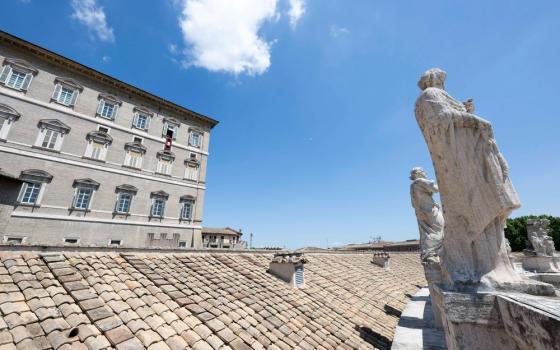 Statues and roof in foreground, and in distance Pope Francis' window with banner. 