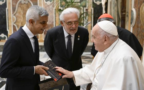 Pope, seated, smiles amid discussion with standing mayor. 