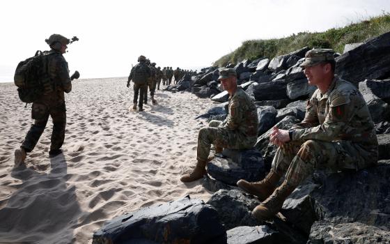 Soldiers sit and walk on beach. 