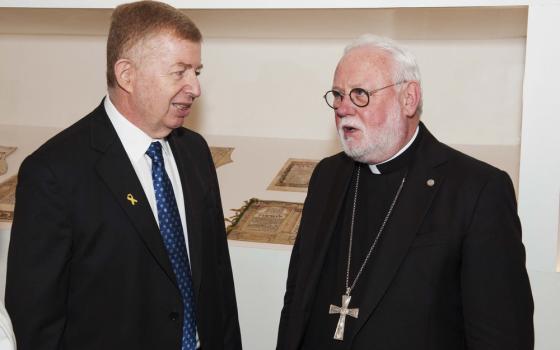 The two men stand facing each other, talking in front of a museum display case