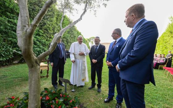 Pope and dignitaries stand around olive tree in garden while speaking