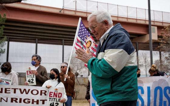 Garcia folds hand in prayer, supporters bearing banners seen in background