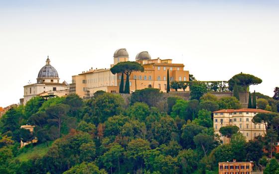 A cluster of large, romanesque buildings sits stop a verdant hill