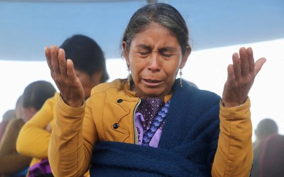 Woman holds hands up, and bows head in prayer. 