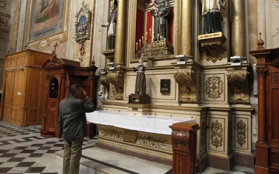 Man stands in front of side altar in ornate church. 