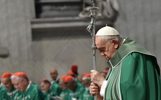 Francis, vested for ordinary time, leans head on crosier while praying. 