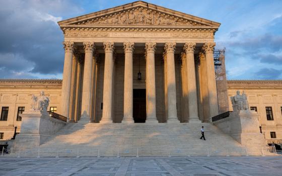 Courthouse looms in the evening light; security guard, dwarfed by building, walks down the stairs. 