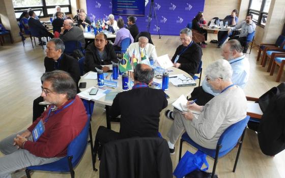 Men and women sit at round tables listening to presentation. 