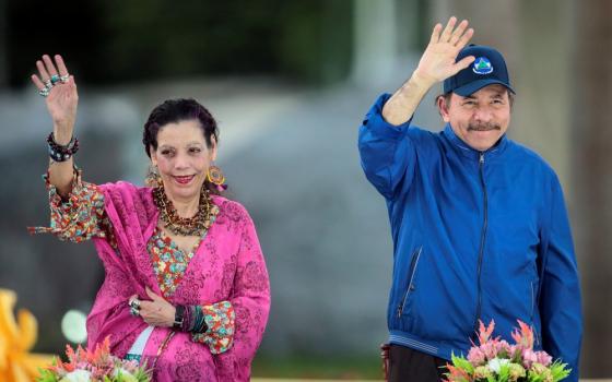 The Presidential couple stand waving and smiling in open air. 