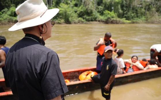 Bishop Seitz pictured from behind, watching migrants disembark from river canoes. 