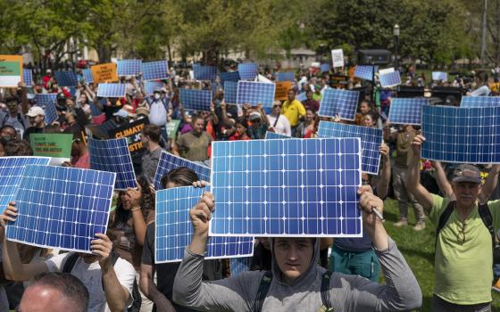 Many people stand assembled holding up solar prints. 