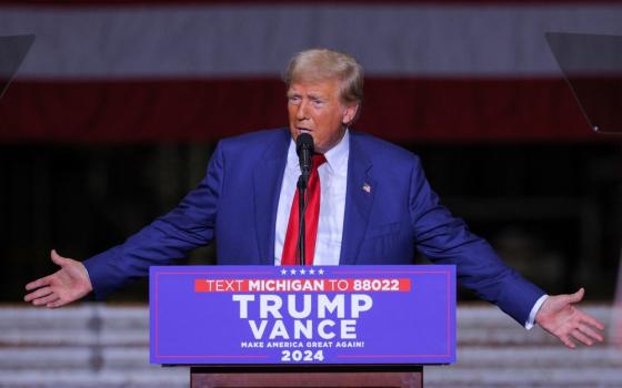 Trump stands at podium, arms opened wide in gesture. 