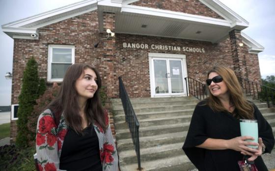 A woman and a younger woman stand in front of a Bangor Christian Schools building.