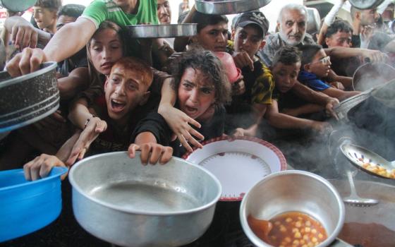 Children holding bowls and pots, their faces marred by deep anguish, clamor one over the other for the food.