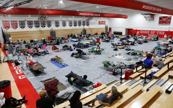 Overhead view of people sleeping on mats and cots in large gym.